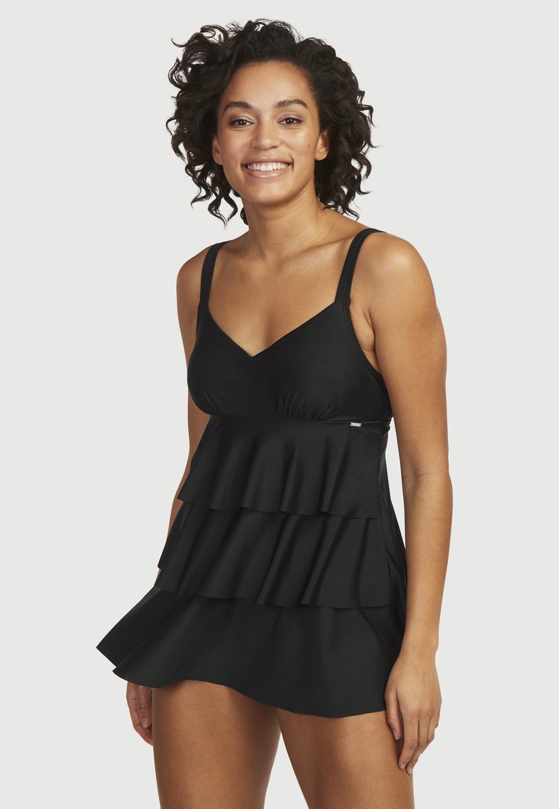 Svart baddräkt med lager av volanger, v-ringning, justerbara band och slät tyg. Midja till låret längd, med en diskret logotypdetalj.