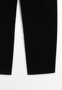 Pantalons en velours côtelé noir avec des côtes verticales, coupe droite et ourlet soigné. Le tissu a une texture douce et un léger éclat.