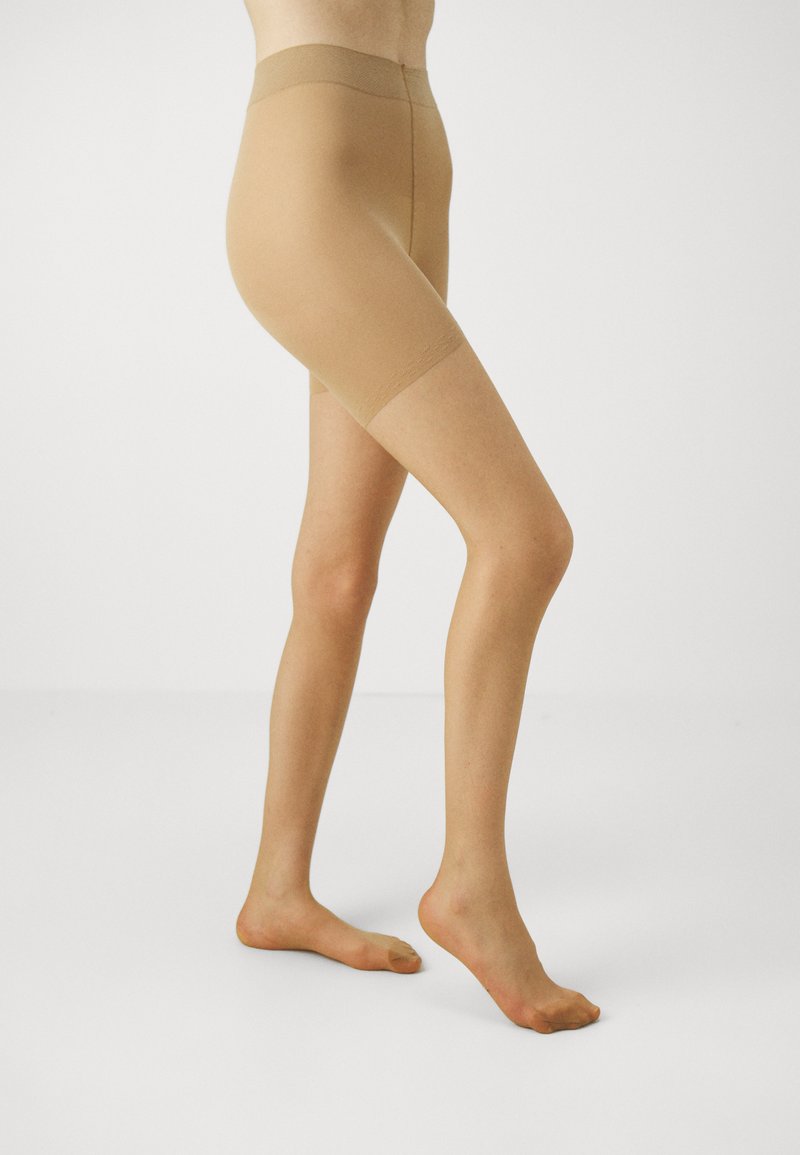 Nude kontrollshorts laget av glatt, semi-transparent stoff, med elastisk midjebånd og design som går til låret med sømløs finish.
