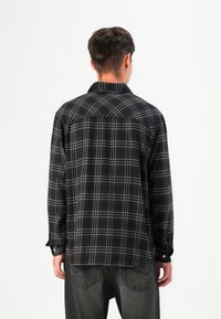 Camisa de cuadros en blanco y negro de manga larga con puños abotonados, fabricada en un tejido suave y con un corte clásico, que presenta un diseño de yugo en la parte posterior.
