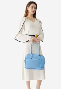 Bolso de mano de cuero azul claro con dos asas cortas, forma rectangular, textura suave y un bolsillo delantero con cremallera.