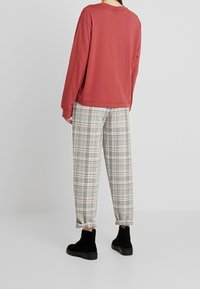 Röd oversized sweatshirt, grå rutiga byxor och svarta ankelboots. Slät tyg, avslappnad passform och byxor med uppvikta kanter.