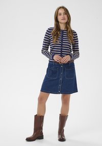 Gestreifte marineblaue und cremefarbene Strickjacke, blauer Jeansrock in A-Linie mit zwei Fronttaschen und braune kniehohe Lederstiefel.