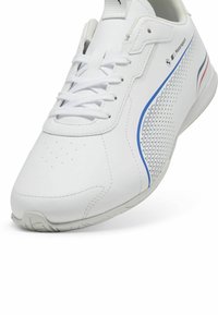 Vit sneaker tillverkad av syntetiskt material, med mesh-accenter, blå och röda ränder samt en texturerad gummisula. Designad för sportigt bruk.