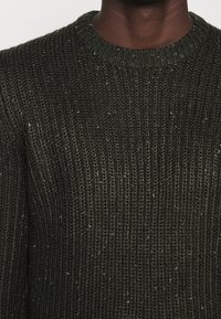 Dunkelgrüner Strickpullover mit gerippter Textur. Verfügt über einen runden Ausschnitt und dezente, helle Sprenkel im gesamten Stoff.