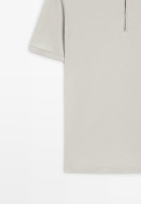 Lyse beige polo med korte ærmer og lynlås ved kraven på hvid baggrund.