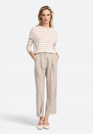 Striped lightweight sweater in beige and cream, paired with light beige trousers featuring front pleats, and flat, light-colored shoes.