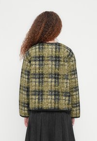 Πράσινο και μαύρο καρό cropped σακάκι με υφή υφάσματος και μαύρη μονόχρωμη επένδυση. Μακριά μανίκια και στρογγυλεμένος λαιμός.