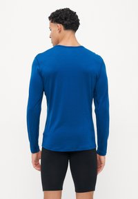Modra dolga majica z dolgimi rokavi, izdelana iz gladkega materiala, z okroglim izrezom, slim fit krojem in stranskimi šivi, kombinirana s črnimi kratkimi hlačami.