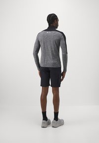 Grå langærmet top med sorte detaljer, struktureret stof; parret med sorte shorts og grå sneakers. Set fra ryggen.