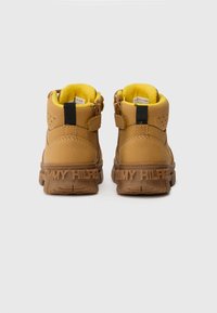 Bottines en cuir marron avec une finition texturée, doublure en polaire jaune, sangle ajustable et "TOMMY HILFIGER" estampé sur la semelle.