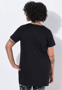 Czarna koszulka z krótkim rękawem o luźnym kroju, z zaokrąglonym dekoltem i gładką fakturą. W połączeniu z legginsami w wzory.