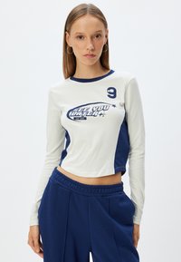 Long-sleeve crop top in cream and navy, featuring a graphic print "SEE YOU LATER," and a round neckline with contrasting trim.