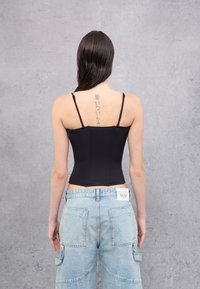 Zwart getailleerd camisole met dunne bandjes, textuurstof, met een verticaal naadontwerp. Gecombineerd met lichtblauwe high-waisted cargobroeken.