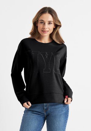 Zwarte sweatshirt met grote "NYC" lettering in een tonale uitvoering. Zacht materiaal met een ontspannen pasvorm en geribde manchetten. Combinatie met blauwe jeans.