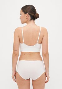 White cotton bralette with thin adjustable straps, paired with matching white cotton briefs. Smooth texture, simple design, no patterns.