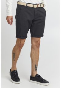 Shorts en coton gris foncé avec des ourlets roulés, dotés de poches latérales et d'une ceinture tissée beige avec des accents marron. Portés avec des baskets noires.