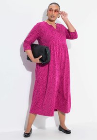 Robe fuchsia avec des rayures zèbre, manches trois-quarts et décolleté en V. Assortie à une pochette noire et des ballerines noires.
