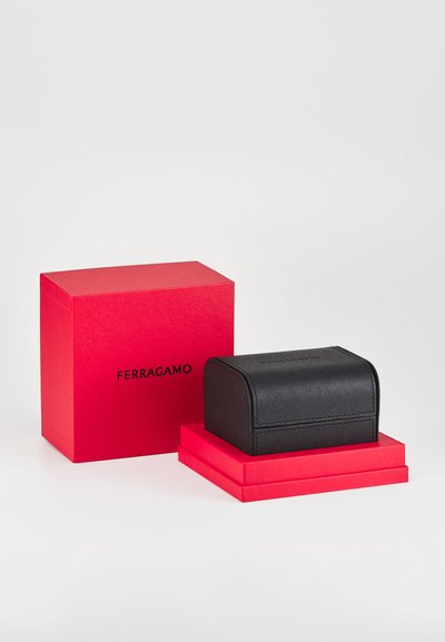 Estuche accesorio de cuero negro con parte superior redondeada, con superficie texturizada, colocado sobre una caja apilada roja con la marca "FERRAGAMO".