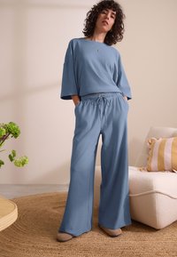 Haut bleu surdimensionné à manches courtes associé à un pantalon bleu à jambes larges avec taille élastique et cordon de serrage. Texture douce, style décontracté.