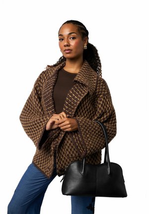 Brązowy, teksturowany, oversize'owy płaszcz z dużym kołnierzem, w parze z dopasowanym brązowym topem, niebieskimi spodniami i czarną skórzaną torebką.