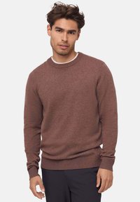 Brązowy sweter z dzianiny z okrągłym dekoltem, ściągaczami na mankietach i u dołu; długie rękawy; miękka tekstura; noszony na białej koszuli.