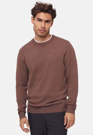 Brązowy sweter z dzianiny z okrągłym dekoltem, ściągaczami na mankietach i u dołu; długie rękawy; miękka tekstura; noszony na białej koszuli.