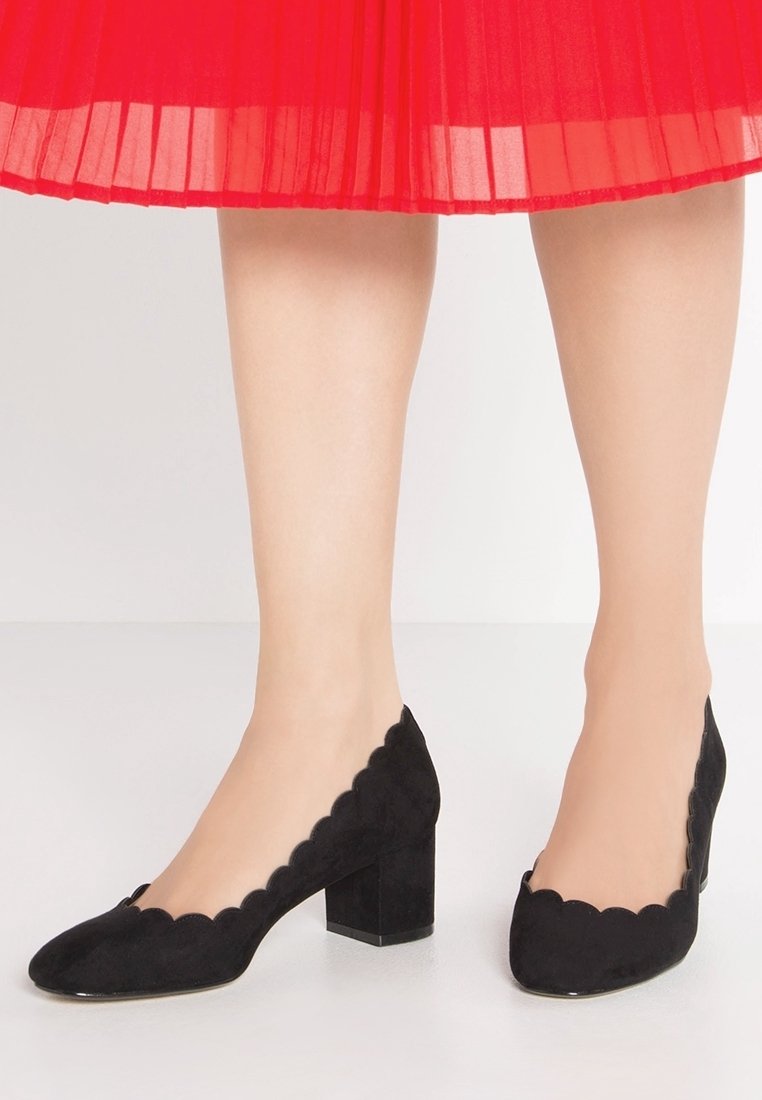 Black suede block-heeled shoes with scalloped edges. The design features a low-cut vamp and a smooth texture.