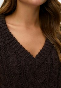 Pull en laine mélangée marron foncé avec un col en V, présentant une texture côtelée et des motifs en torsades sur le tissu.