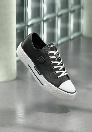 Black leather sneaker with white accents, textured rubber sole, and logo. Features traditional lacing and a rounded toe with a distinctive design.