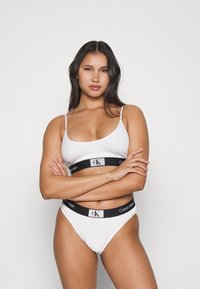 Hvit bh og matchende truser med en svart Calvin Klein-logo på livet. Slank, glatt stoff, justerbare stropper og tettsittende design.