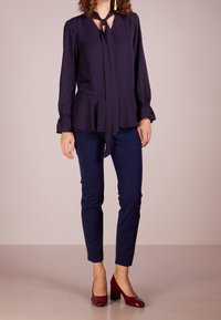 Marinblus med röda prickar, knytkrage, utsvängda ärmar och peplumslut, kombinerad med marinblå figurnära byxor och burgundy klackskor.