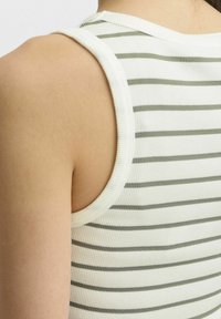 Pruhovaný tílko s ribbed texturou; má bílou barvu s tenkými olivově zelenými pruhy a kulatým výstřihem, který zvýrazňuje přiléhavý střih.