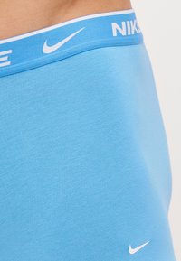 Modré boxerky Nike vyrobené z mäkkej bavlnenej zmesi, s jemným modrým pásom a bielym textom „Nike“ a logom na boku.