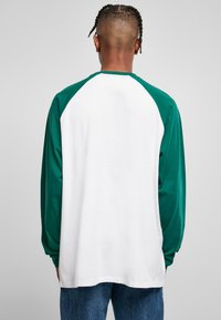 Langarmshirt mit grünem Raglan-Design, weißem Oberteil, weichem Baumwollmaterial, geradem Saum und lockerer Passform.