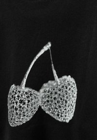 Svart skjorta med en vit grafik av två körsbär med intrikata mönster och prickar, som betonar textur och kontrast.