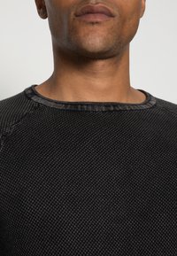 Schwarzer, strukturiertes Crewneck-Sweatshirt mit geripptem Kragen, das über feine Musterdetails und verstärkte Nähte an den Schultern verfügt.