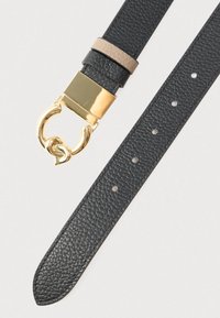 Juodas odinis diržas su struktūruotu paviršiumi, auksinės spalvos sagtimi ir smėlio spalvos odos akcentu prie sagties. Skylutės dydžio reguliavimui.