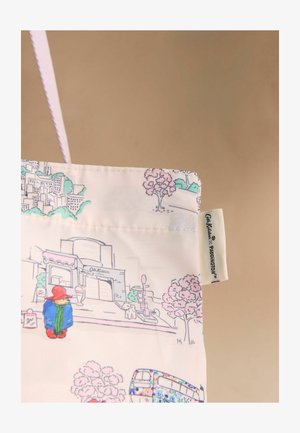 Piros kalapos és kék kabátos Paddington Bear rajzolt mintája, fák, egy kutya, egy busz és épületek mellett egy krémszínű vászontáskán, vászon fogóval.