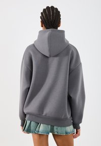 Sudadera gris con capucha de corte relajado y puños acanalados, combinada con una mini falda de mezclilla acampanada que presenta un dobladillo plisado.