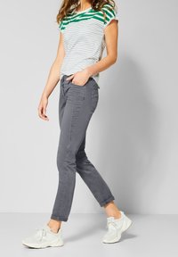 Pantalones grises ajustados con puños enrollados, combinados con una camiseta a rayas verde y blanca. El atuendo se completa con zapatillas blancas.