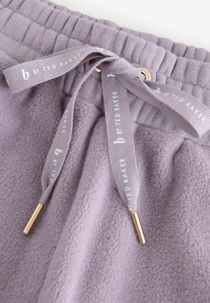 Lilac krāsu flīsa bikses ar ribotu vidukli, kas aprīkotas ar auklu ar zeltainiem galiem, uz kurām ir uzraksts "b by Ted Baker." Mīksta tekstūra.
