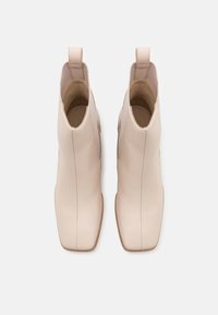Würfelförmige Knöchelstiefel aus weichem beigen Leder mit verlängerten, quadratischen Zehen und minimaler Nahtdetails. Mit Anziehhilfen für ein einfaches Anziehen.