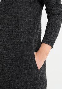 Szara teksturowana dzianinowa sukienka z długimi rękawami, boczną kieszenią i luźnym krojem. Materiał ma puszystą fakturę, co zwiększa poczucie ciepła.