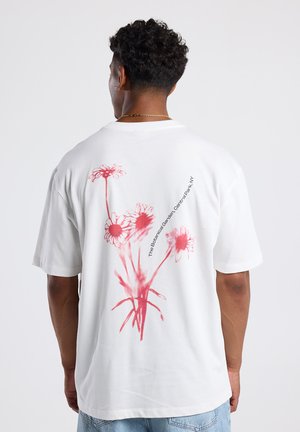 T-shirt en coton blanc à manches courtes, arborant un design floral rouge à l'arrière et le texte "Le Jardin Botanique, Compton Park, NY."