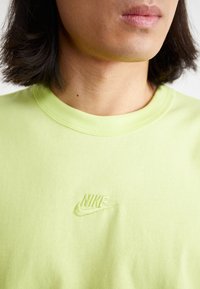 Närbild av en person som bär en ljusgrön Nike-tröja med en broderad logotyp på bröstet, där den nedre delen av ansiktet och nacken syns.