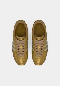 Zlaté tenisky s perforovaným koženým zvrškom, béžovými pruhmi a zodpovedajúcimi šnúrkami. Textúrovaná vnútorná časť s logom. Dizajn zaoblených špičiek.