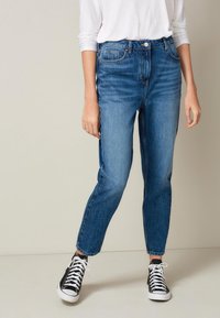 Vaqueros de mezclilla de cintura alta en azul claro con un corte recto, que presentan un diseño de cinco bolsillos y un leve desvanecimiento. Combinados con zapatillas negras de caña alta.