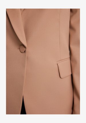 Jasno-beżowa marynarka o gładkiej, teksturowanej tkaninie, z okrągłym zapięciem na guzik, wykładanym kołnierzem i jedną kieszenią po boku.