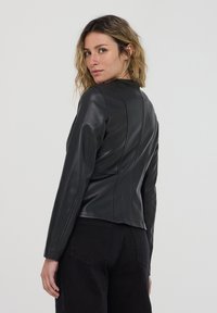 Giacca di pelle nera con un design aderente, maniche lunghe e dettagli delle cuciture evidenti. Indossata con pantaloni neri, vista da dietro.